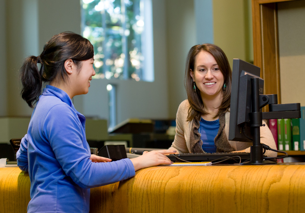 Librarian helping student with research at service desk