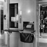 A vertical machine with a chute that conveys books and a slide from which books fall into a fabric bag.