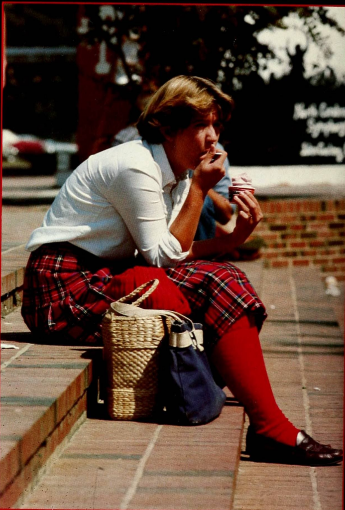 Student wearing a plaid skirt, long red stockings and loafers eating frozen yogurt. 1990.