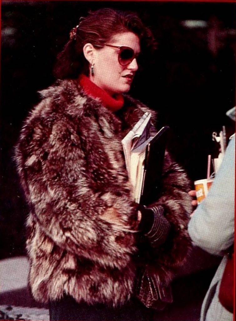 Student wearing sunglasses and a large fur coat holding books. 1990.