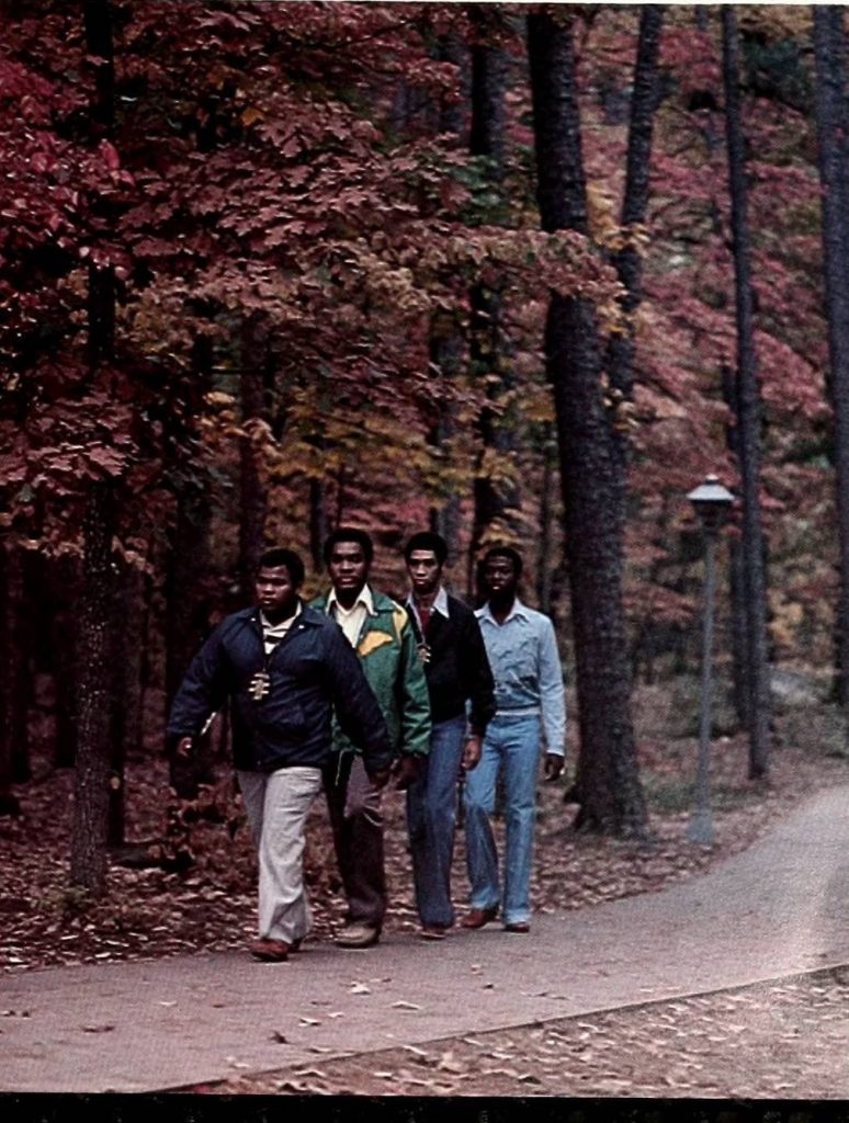 Four students walking across campus with Fall trees behind them. 1990.