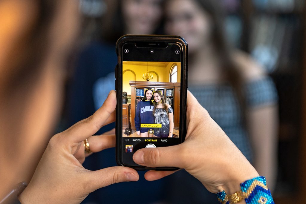 A person takes a photo of two graduating students with an iphone