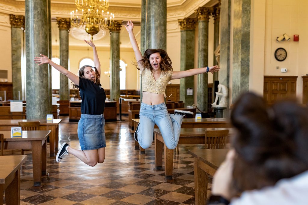 Two students jumping with hands in the air in the fearrington reading room of Wilson Library