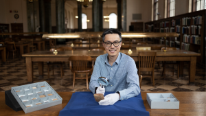 Joseph Lam pictured in Wilson library with cuneiform tablets and a magnifying glass