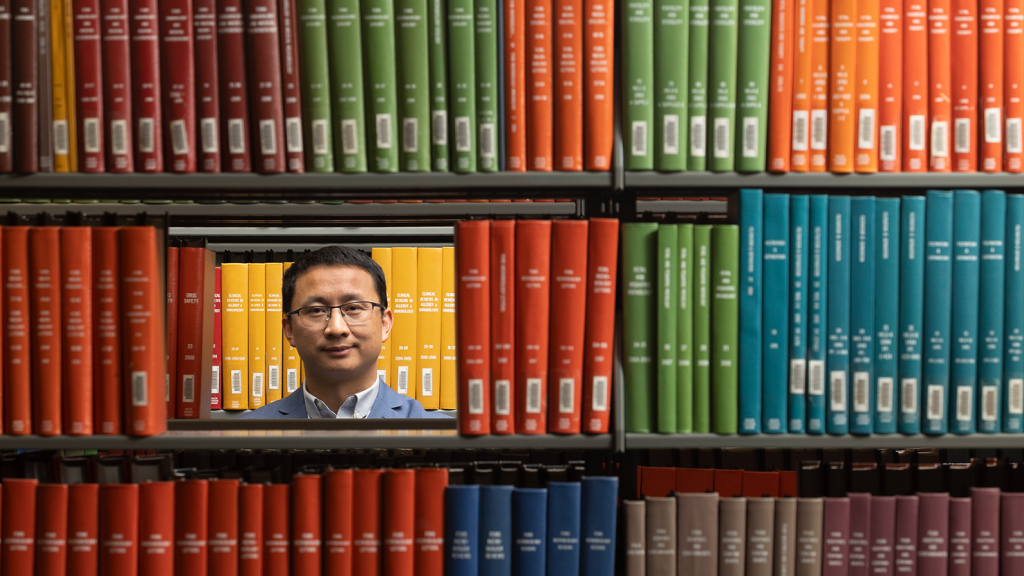 Weiming Tang pictured through a space in books on a shelf