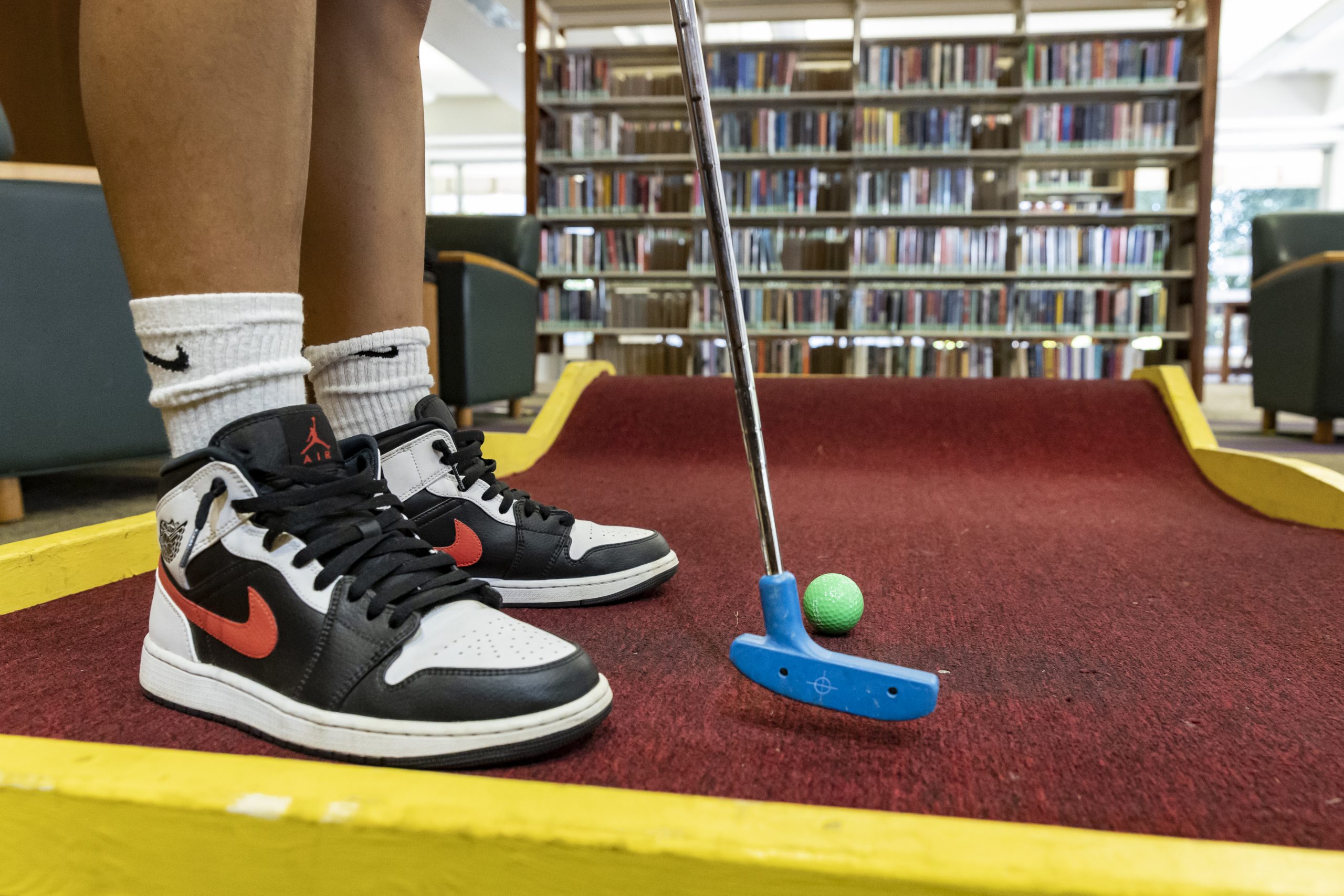 Close up of air jordan sneakers and a golf putter hitting a golf ball in mini golf