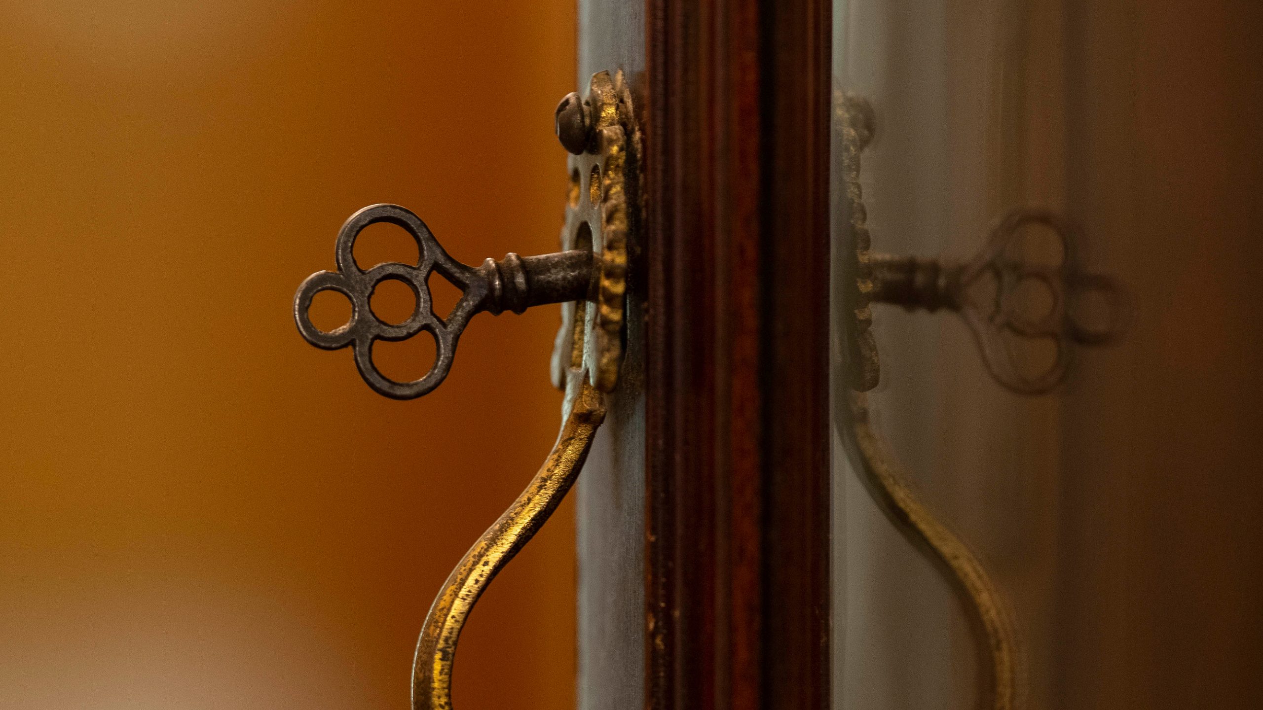 A small key is inserted into a brass lock on an antique exhibit cabinet.