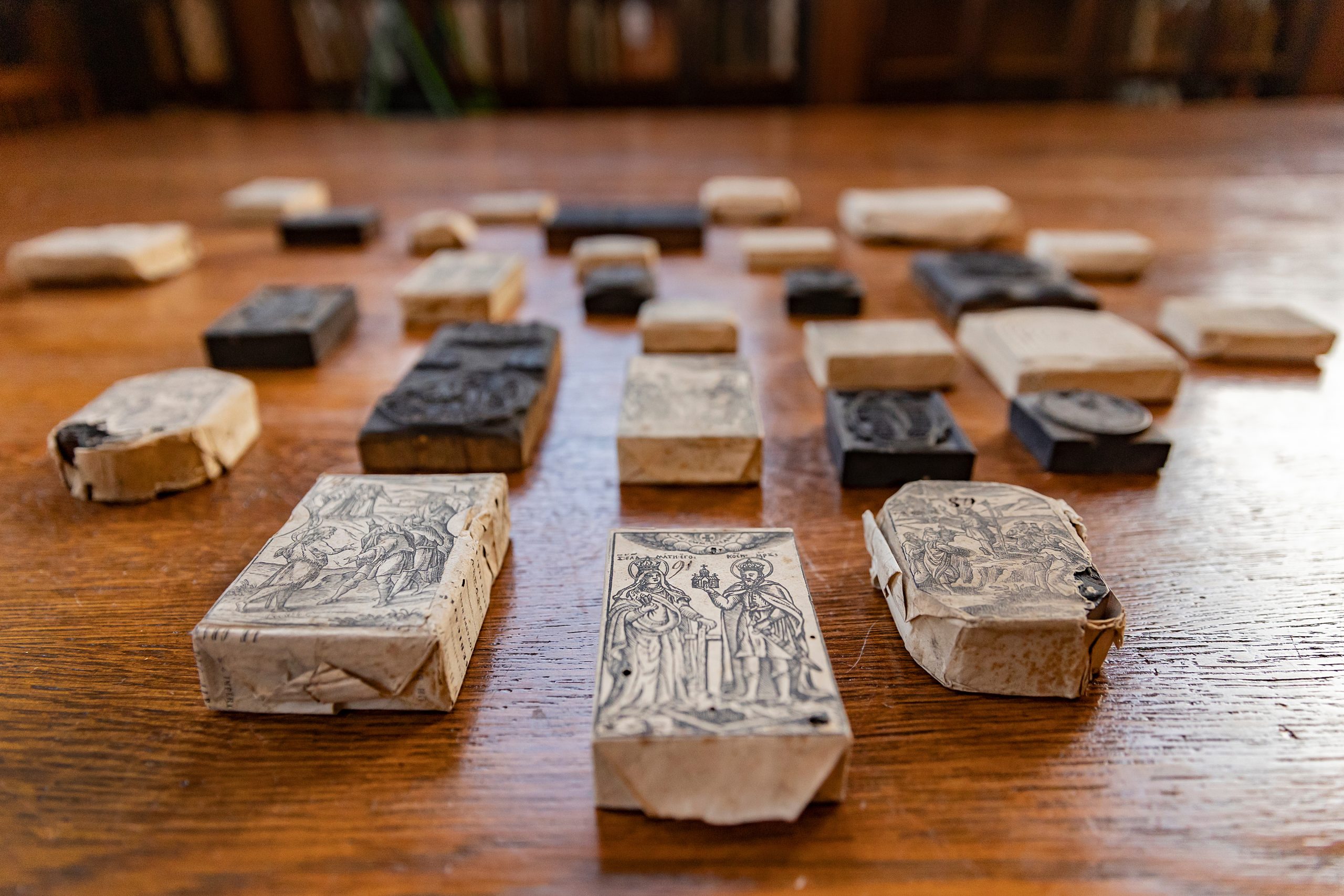 A series of woodblocks are lined up on a wooden table in the Fearrington Reading Room. Each block depicts a unique image. Some blocks are covered in paper wrappings.