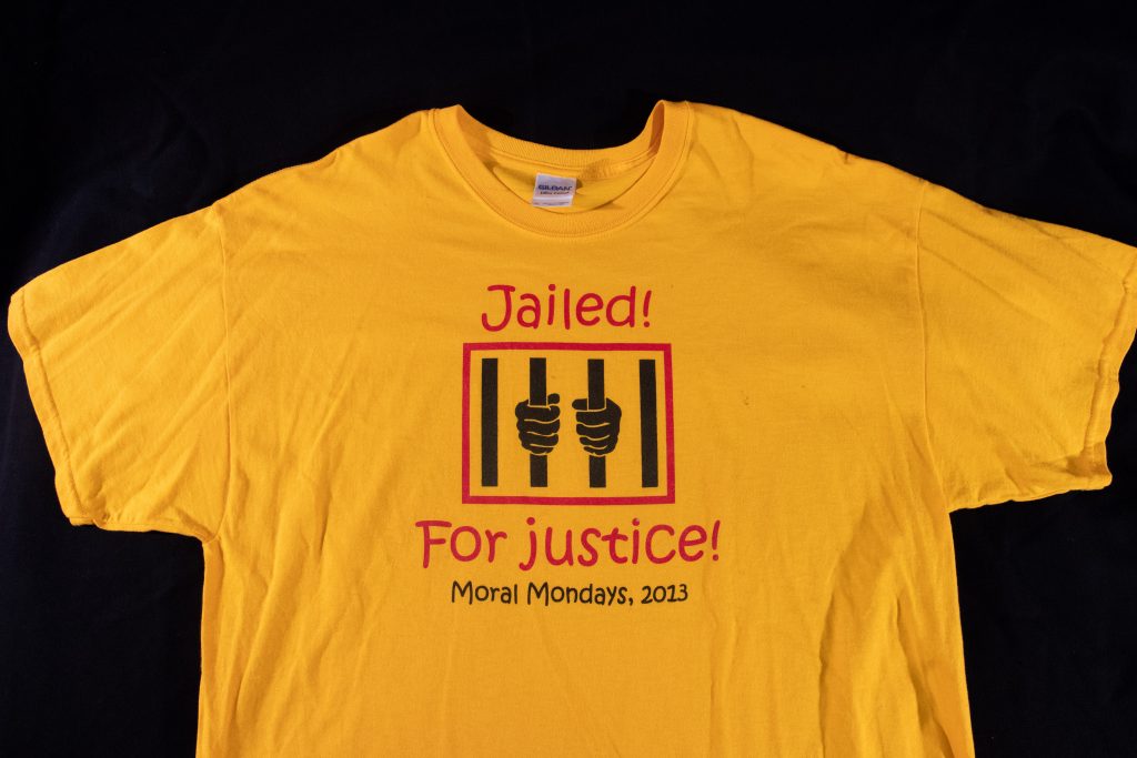 Bright yellow t shirt with the text "Jailed For Justice Moral Mondays 2023'