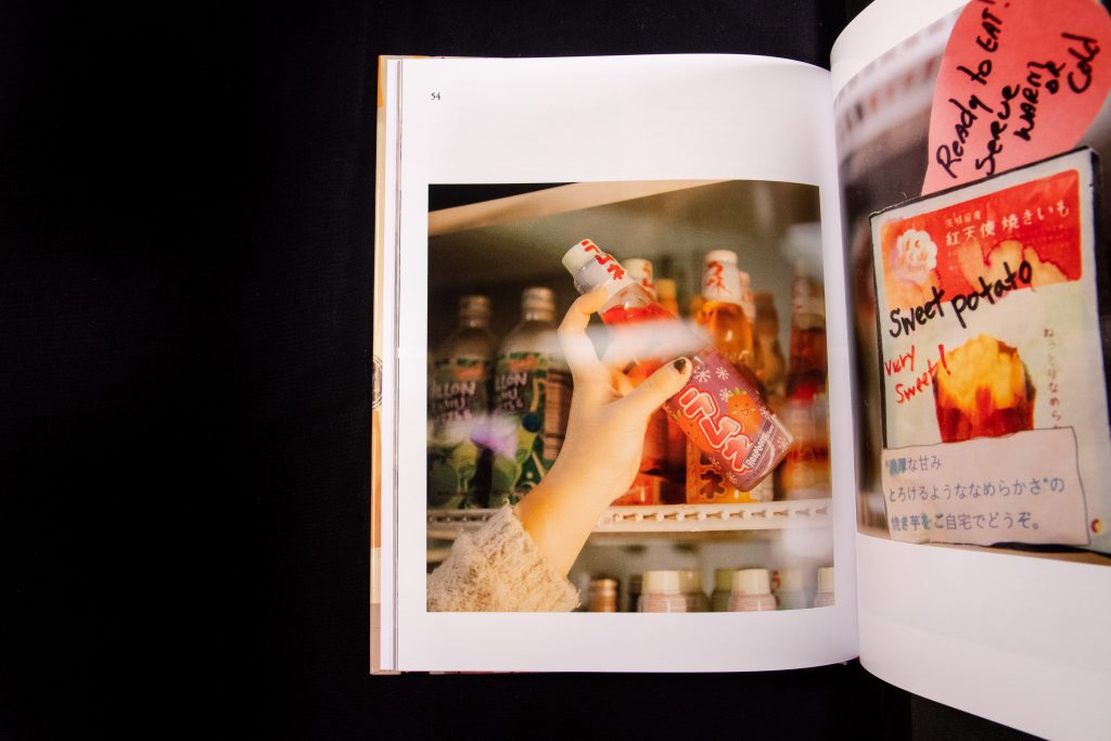 Open photo book showing a color photo print of a hand reaching for a soda on a shelf in a store.