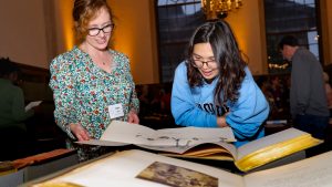Two people leaning over a large volume in the Fearrington Reading Room during Recent Acquisitions Evening
