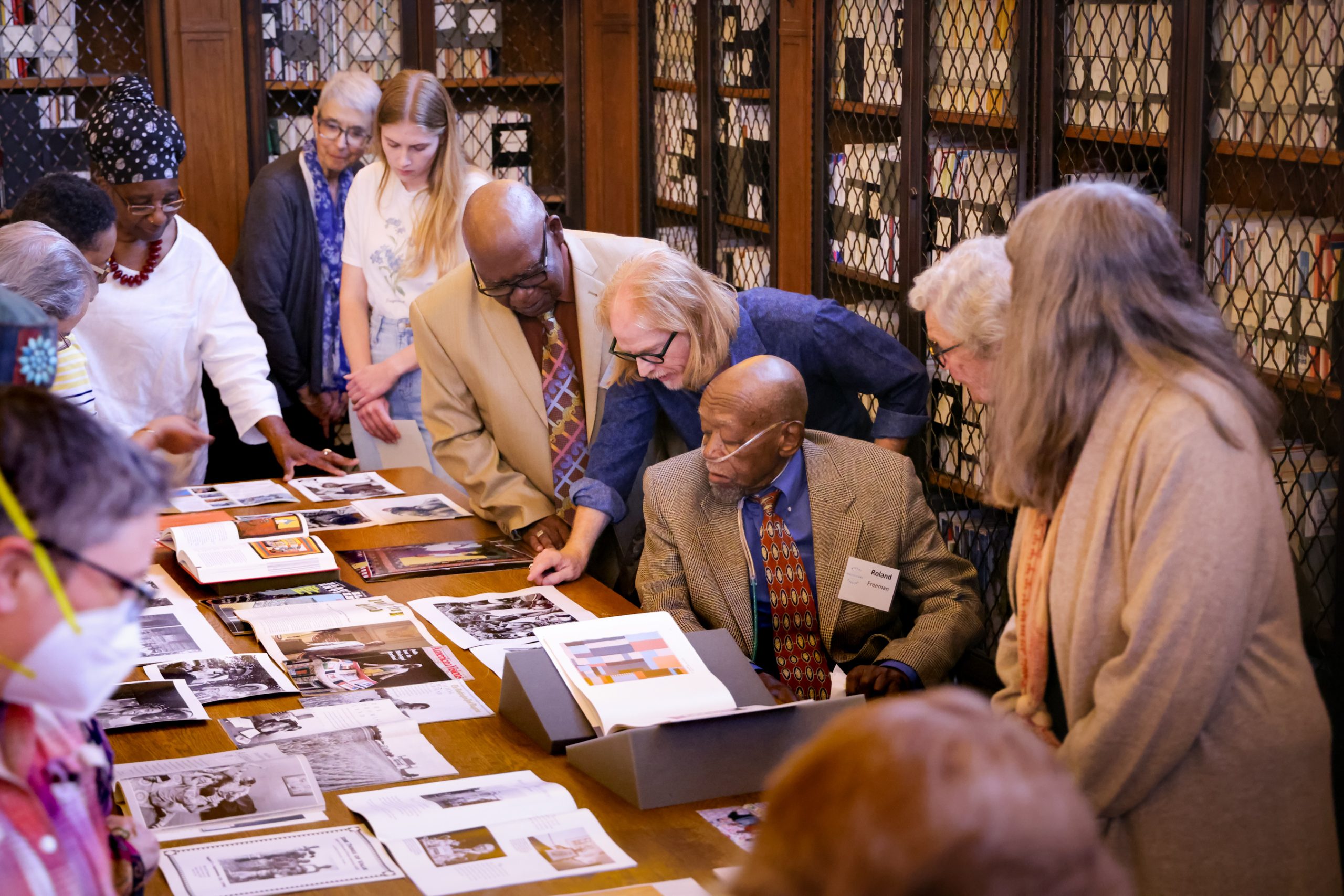A group of people, including Roland Freeman, huddle around a table looking at photographs.Recent Acquisitions Evening on April 27, 2023 in Wilson Special Collections Library, UNC-Chapel Hill.