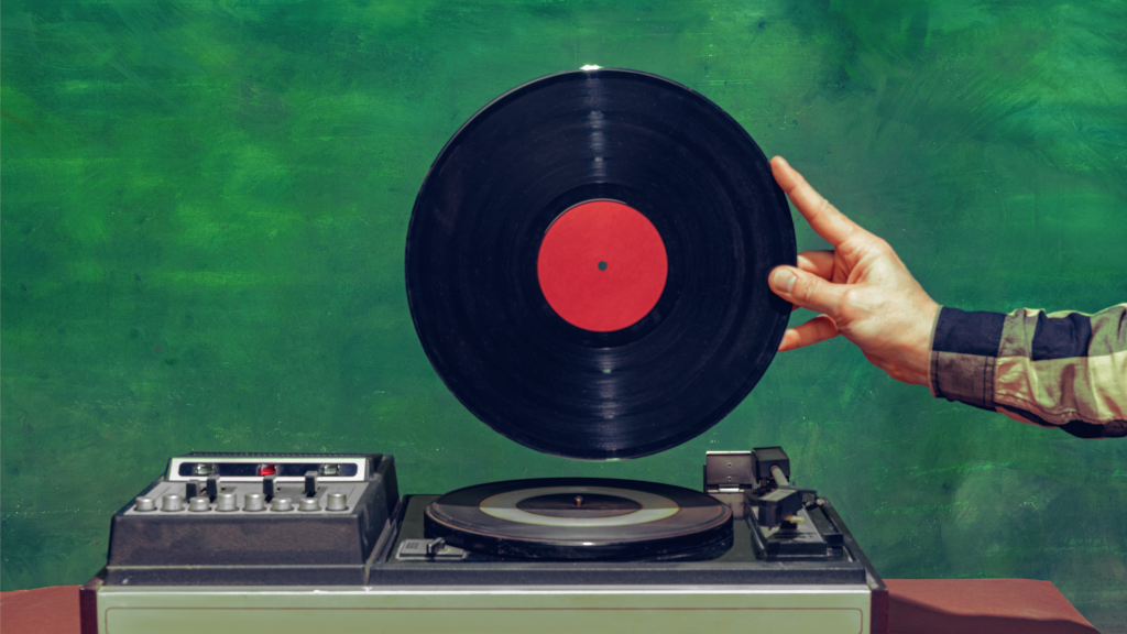 A hand holds a vinyl record above a turntable.