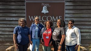 Group photo of women standing in front of a building with a sign that says Penn Center Welcome
