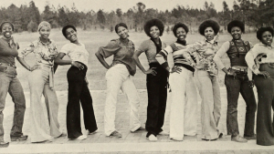 A group of black women pose for a photo, each with a hand on her hip.